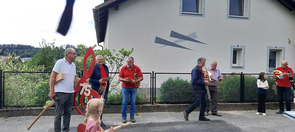 Einige Personen mit Instrumenten und ein Mann mit einem großen Notenschlüssel als Überraschungsgeschenk.