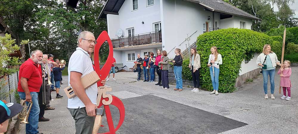 Mehrere Personen mit Instrumenten in einem Spalier aufgestellt. Im Vordergrund ein Mann mit einem großen Notenschlüssel.