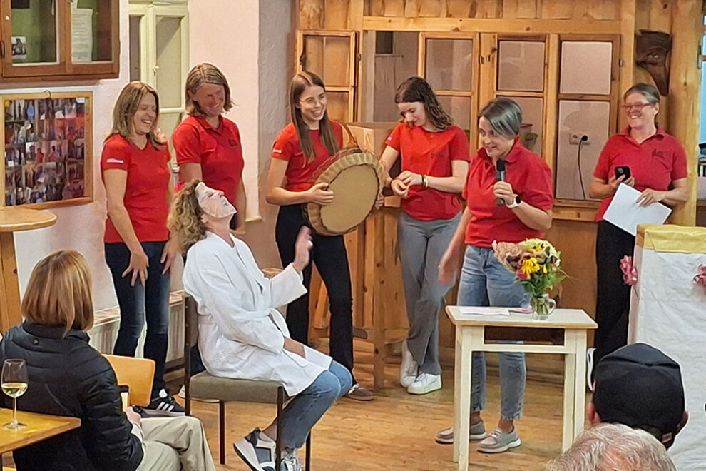 Mehrere Personen stehen hinter einer Dame, die auf einem Sessel sitzt und eine Gesichtsmaske trägt